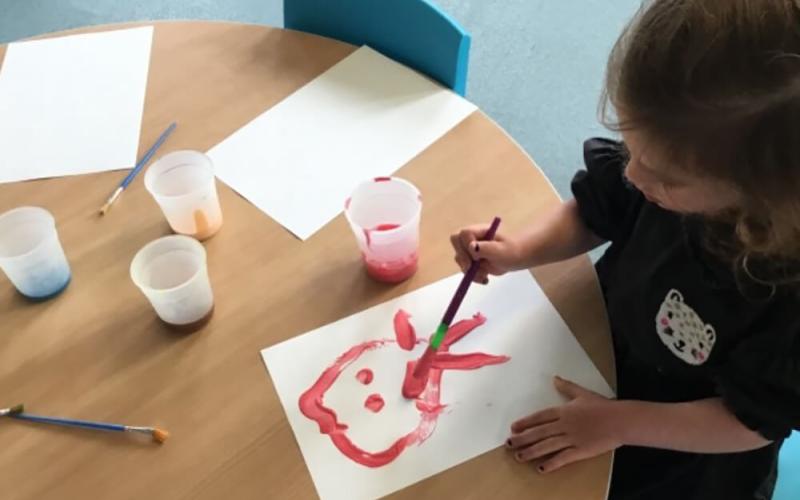 Child painting a stick person in red paint