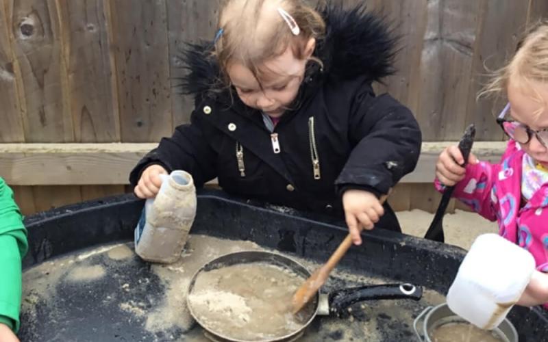Child mixing sand and water in a frying pan